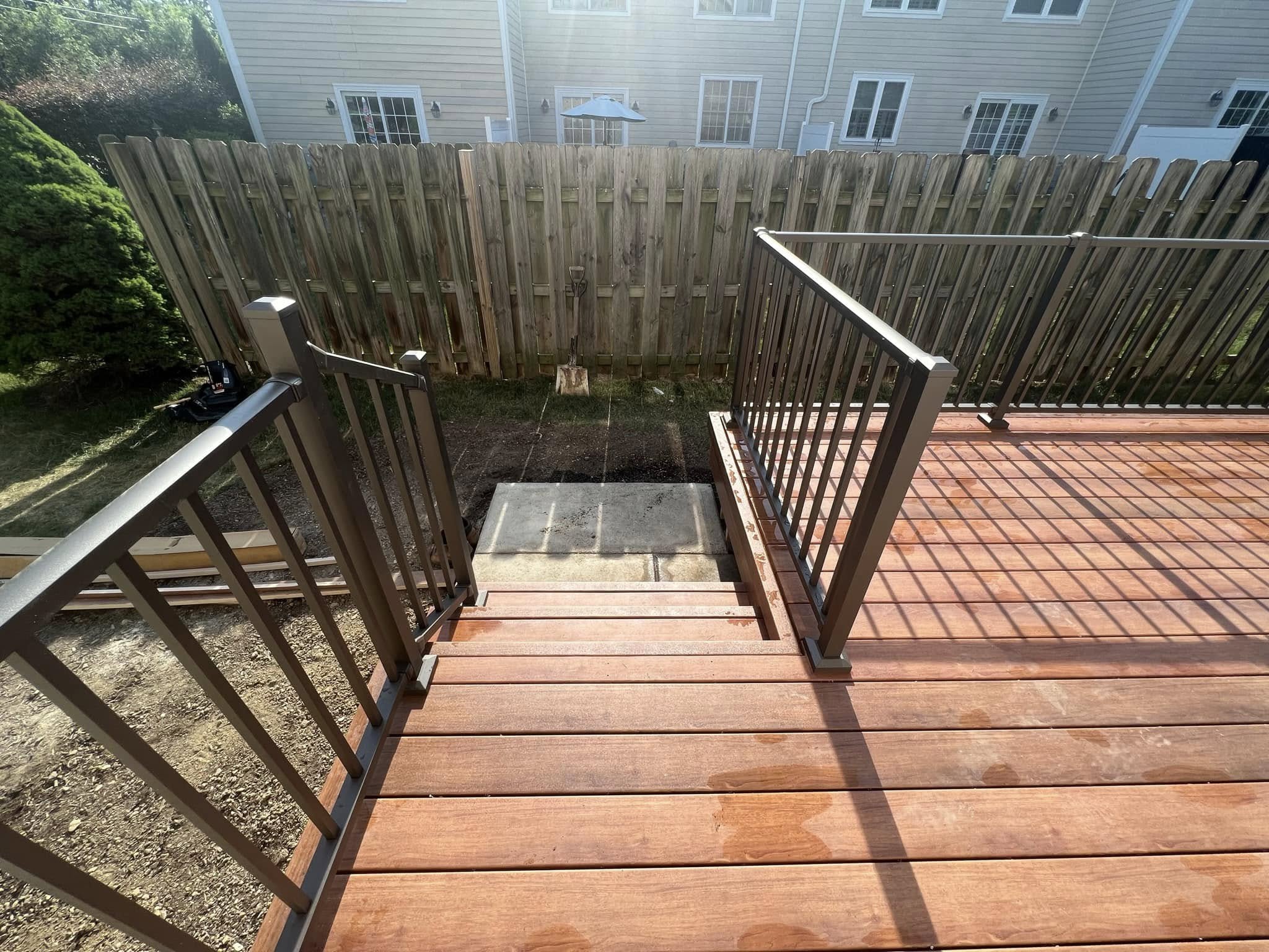 Wood deck stairs with dark railings leading down to a concrete landing